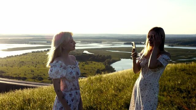 Two cute blonde young women taking pictures of the phone standing on the hill above the highway