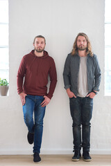 Portrait of twin brothers standing by a wall together in studio. Young twins, siblings and family of young men side by side. Relationship with brother, brotherhood and two guys who look identical - obrazy, fototapety, plakaty