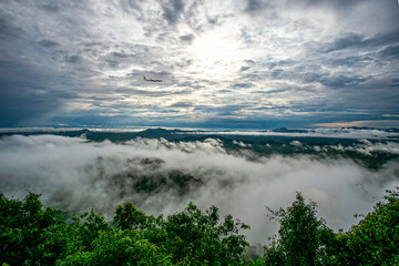 The mist above the mountain peaks and the plane flying in the distance and the gray background clouds.