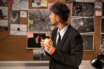 Detective looking at evidence board in office and eating fast food hamburger, workplace food