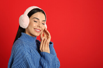Beautiful young woman wearing earmuffs on red background. Space for text