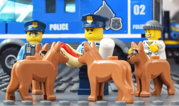 Lego minifigures of police officer with hotdog and four hunger dogs. Editorial illustrative image of law and punishing. Studio shot.
