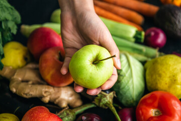 Close-up, an apple in a female hand on a blurred background with vegetables.