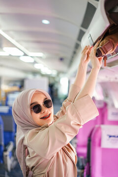 Beautiful muslim female traveler passenger putting her hand luggage on overhead locker before takeoff.