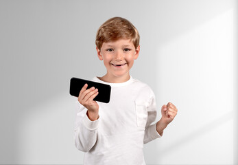 Fototapeta premium Happy boy with fist and smartphone in hand, copy space white bac