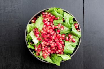Healthy food pomegranate vegetable salad in bowl on black wood background.