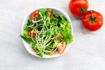Healthy food sunflower sprout salad has leave lettuce vegetable tomato in bowl on white wood background.
