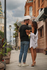 Young couple with umbrella enjoying time together under rain on city street