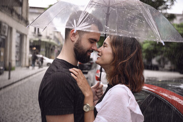 Young couple with umbrella enjoying time together under rain on city street