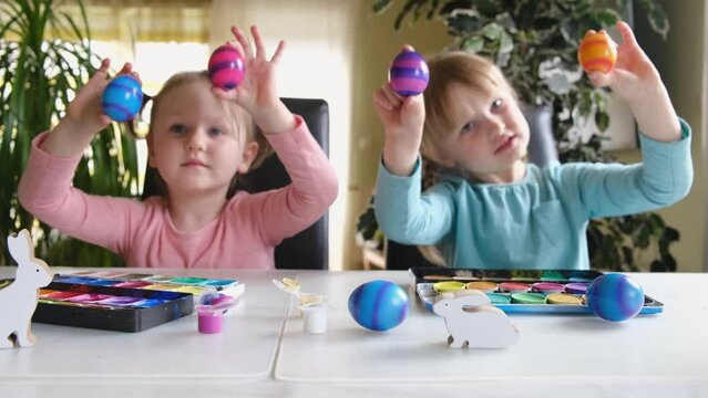 Happy preschool cute kids having fun looking into the camera making crazy funny face with colored Easter eggs at home.