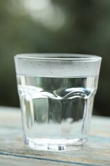 Glass of pure water on light blue wooden table against blurred background, closeup