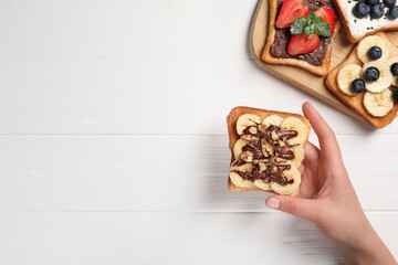 Woman holding delicious sweet toast at white wooden table, top view. Space for text
