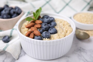 Bowl of delicious cooked quinoa with almonds and blueberries on white marble table, closeup