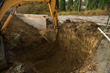 Fototapeta na wymiar A road excavator dredges the hole near the family house 