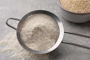 Sieve with quinoa flour on light grey table, closeup