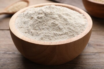 Quinoa flour in bowl on wooden table, closeup
