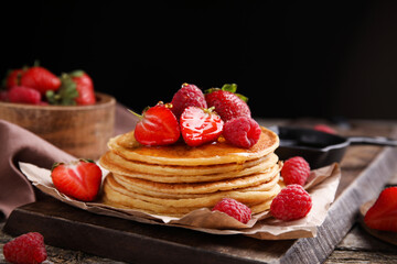 Tasty pancakes with fresh berries and honey on wooden board, closeup