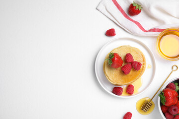 Tasty pancakes served with fresh berries and honey on white table, flat lay. Space for text
