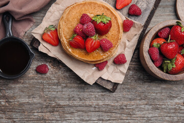 Tasty pancakes served with honey and berries on wooden table, flat lay. Space for text