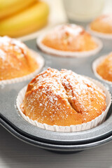 Tasty homemade banana muffins powdered with sugar in tray on white wooden table, closeup