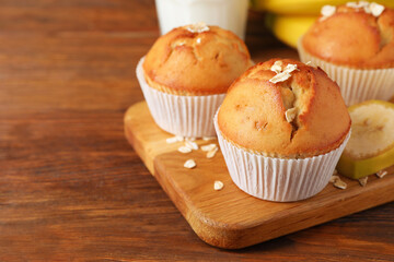 Tasty muffins served with banana on wooden table. Space for text