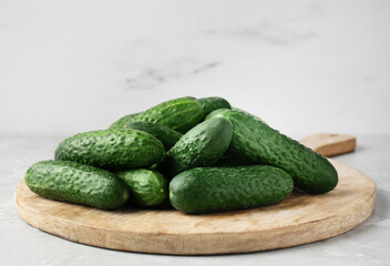 Board with fresh ripe cucumbers on white marble table