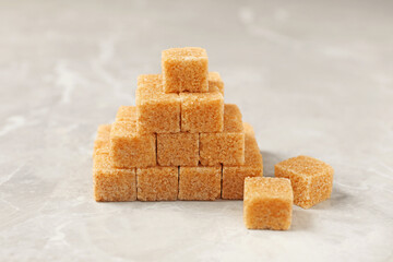 Pyramid made of brown sugar cubes on light grey marble table, closeup