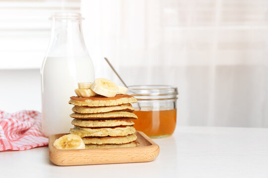 Plate of banana pancakes with honey and milk on white wooden table. Space for text