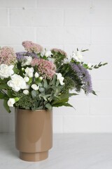 Ceramic vase with beautiful bouquet on light table near white brick wall