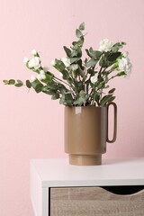Stylish ceramic vase with beautiful flowers and eucalyptus branches on white table near pink wall