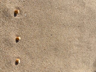 three cigarette butts arranged as bullet points in sand on beach