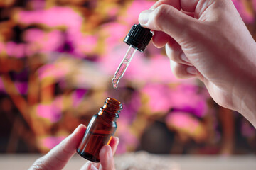 Hands holding a bottle of CBD oil and its dropper lid, with hemp leaf in the background. Legalized...