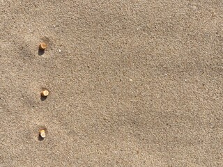 three cigarette butts arranged as bullet points in sand on beach