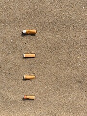 Four cigarette butts arranged as bullet points in sand on beach