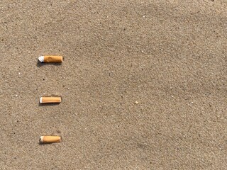 three cigarette butts arranged as bullet points in sand on beach