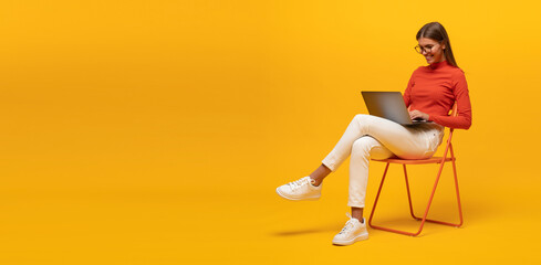 Portrait of woman working on laptop sitting on chair isolated on yellow banner background