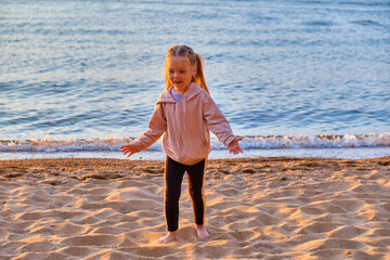 A little girl plays on the shore of the Barguzin Bay of Lake Baikal during a bright sunset. Republic of Buryatia, Russia.