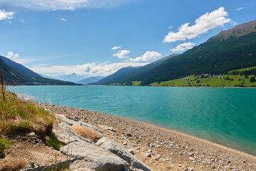 Shore at Reschen lake in italy. Blue water surrounded by high mountains against blue cloudy sky. Italy, Lake Resia, Vinschgau, Giern.