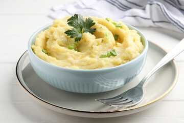 Bowl of tasty mashed potatoes with parsley and green onion served on white wooden table, closeup
