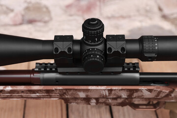 Closeup view of modern powerful sniper rifle with telescopic sight on blurred background