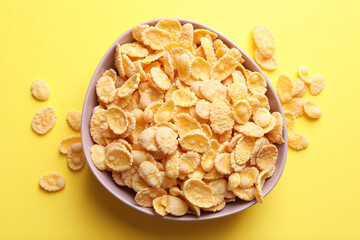 Bowl of tasty crispy corn flakes on pale yellow background, flat lay