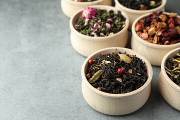 Different kinds of dry herbal tea in wooden bowls on light grey table. Space for text