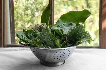 Different herbs in colander near window indoors