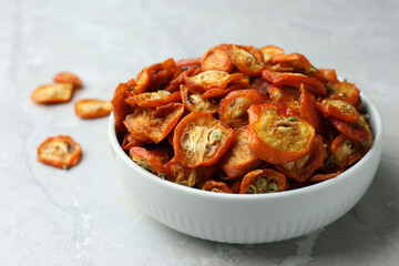 Bowl with cut dried kumquat fruits on white marble table, closeup