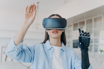 Disabled girl in virtual reality glasses touching air by bionic prosthetic arm. Medical high tech