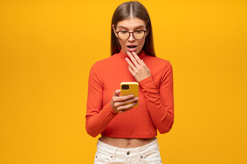Girl learning shocking news from social media reading post on her phone on yellow background