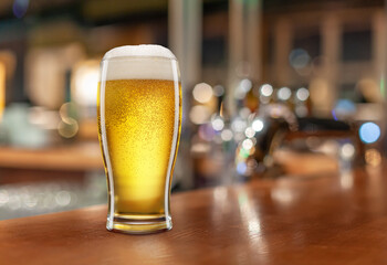 Glass with light beer on a wooden table against the backdrop of a dark pub. Beer vintage concept.