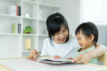 Fototapeta na wymiar single mom happy together with baby. Asian young mother smile with daughter in home. mom reading book having fun and jok with her kid. teaching, Home School, preschool