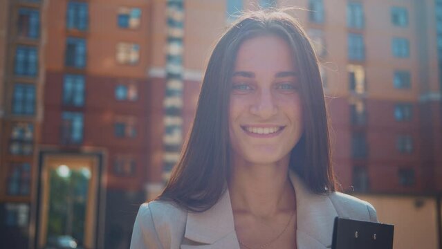 Closeup portrait of successful lady, symbol of career and success. Smiling business woman look at camera. Background of city buildings. Urban lifestyle profession concept, modern life. Slow motion