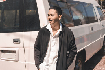 A local civilian guy wearing a white polo shirt and black jacket standing beside a white van as...